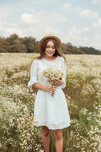 美丽的女人在白色礼服与野生甘菊花花束在草地上的肖像