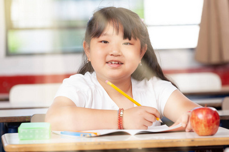 在小学的亚洲女小学生, 在她的办公桌上快乐, 从外面来的太阳光线