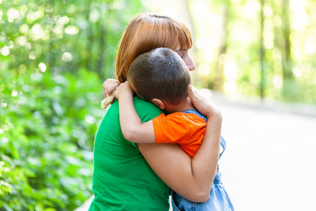 美丽的女人和她的小儿子颤抖着, 强烈拥抱, 在城市公园的背景.
