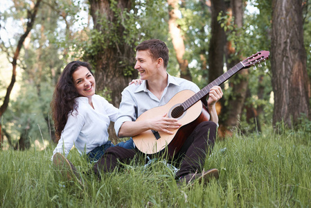 年轻夫妇坐在森林里玩吉他, 夏天自然, 阳光明媚, 阴影和绿叶, 浪漫的感觉