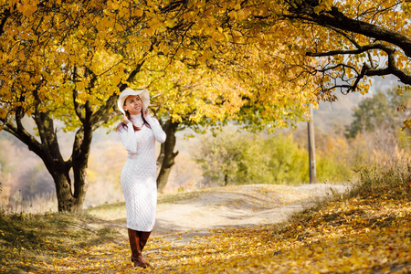 秋天叶子背景的礼服和帽子的妇女