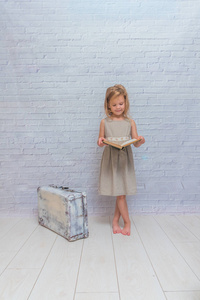 女孩, 婴儿穿着白色砖墙背景与手提箱, 与书