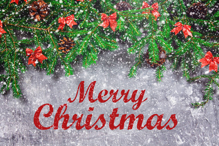 冷杉枝具圆锥和红色弓在灰色具体背景之上。新年圣诞节。圣诞快乐