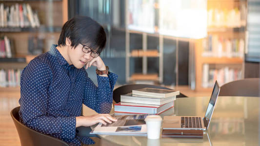 年轻亚洲人学生阅读的书和杂志在公共图书馆 教育研究和自学习在大学生活概念