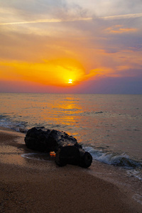 日落时美丽的大海。在黄色的太阳背景下喷洒和石头。海景