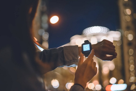 妇女的部分看法与 smartwatch 在手腕和夜城市灯在背景