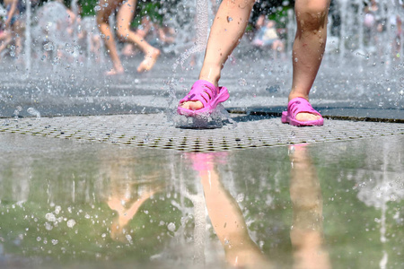 一个穿着粉红色拖鞋的湿腿女孩在夏天在城市公园的喷泉里玩耍.照片
