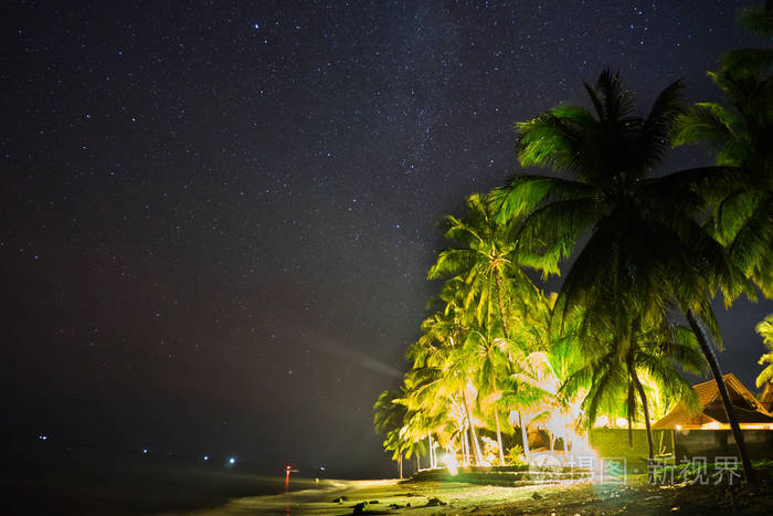 夜空中的星星与房子和棕榈树在海滩上