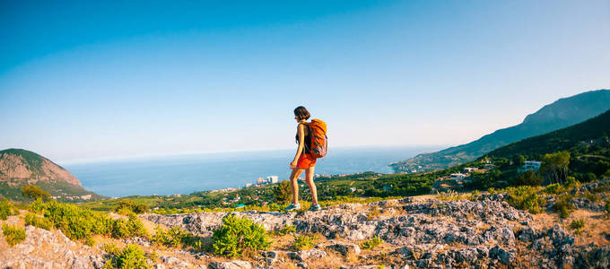 女孩在山顶上。一个背着背包的女人沿着一条山路走。爬上山顶。旅行到风景如画的地方。游客对天空和海
