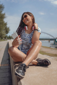 快活的年轻妇女听音乐从智能手机在河岸