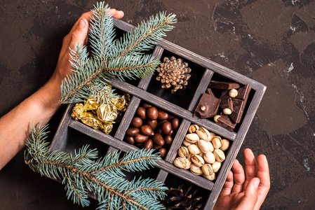 黑暗背景下的圣诞作文。装饰木箱与坚果, 糖果在金色包装, 一块巧克力, 锥和几个世纪的云杉。手捧礼物