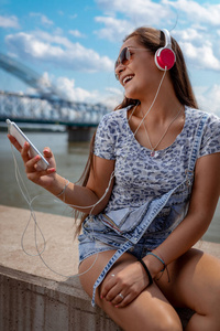 快活的年轻妇女听音乐从智能手机在河岸