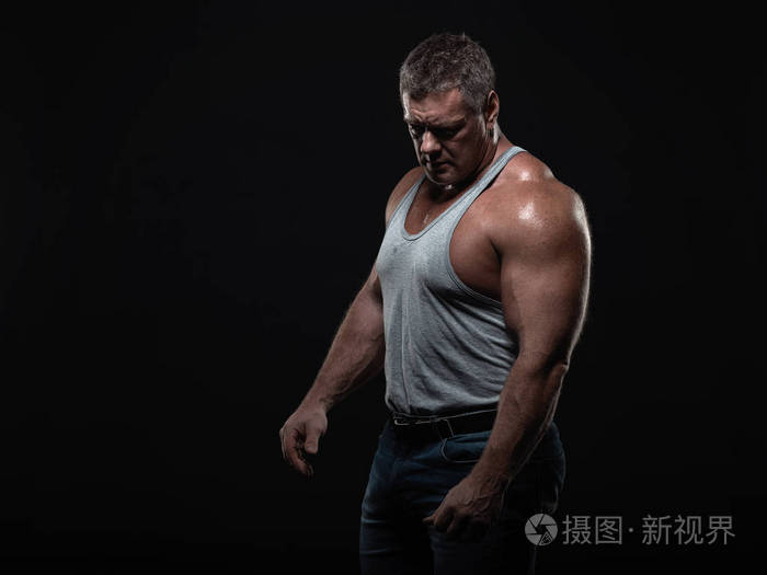 强大的肌肉健美运动员摆在黑色背景.力量与健康的概念