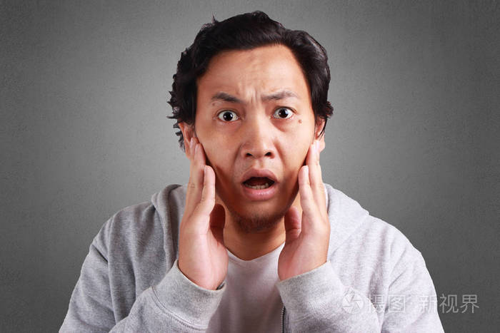 年轻的亚裔男子身穿白衬衣和灰色夹克, 表情震惊, 嘴巴张开.背景灰色.