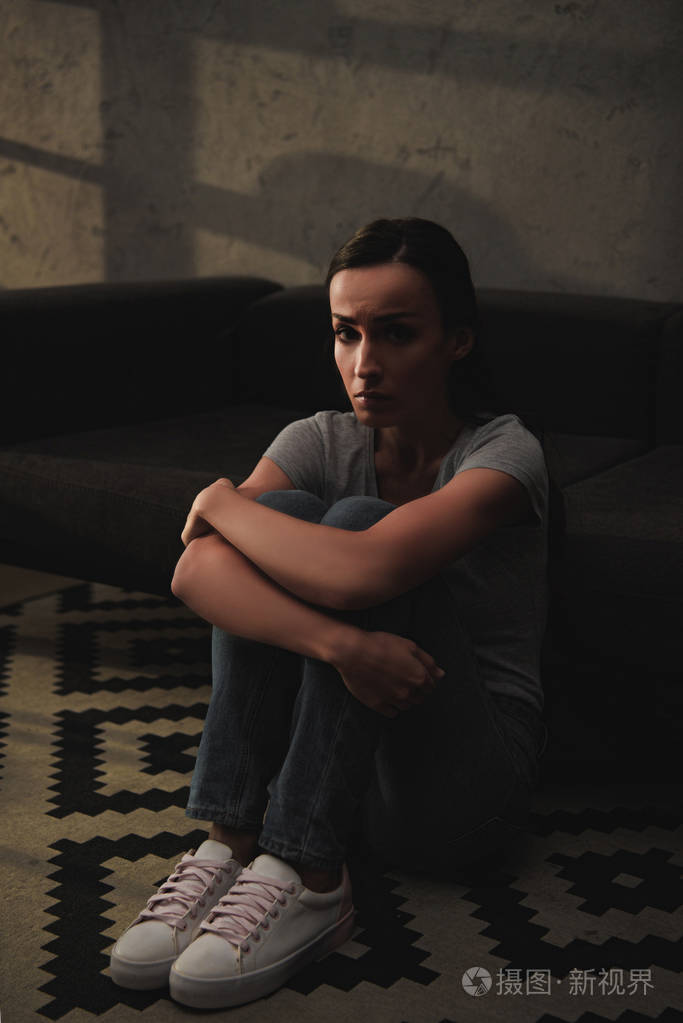 沮丧的妇女抱着她的膝盖, 而坐在地板上在家