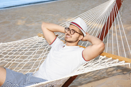 一个年轻人在海边的吊床上休息。暑假