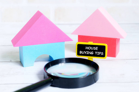 在白色木质背景下, 用房子模型和放大镜来写与房子购买技巧的黄色黑板的选择性焦点。房地产主题