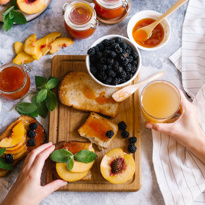 用杏果酱和新鲜水果和白色木桌上的树叶敬酒。美味早餐