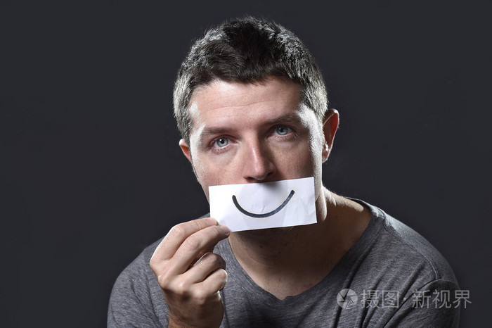 年轻人沮丧迷失在痛苦和悲伤在他嘴上在抑郁症概念持有纸用笑脸的人