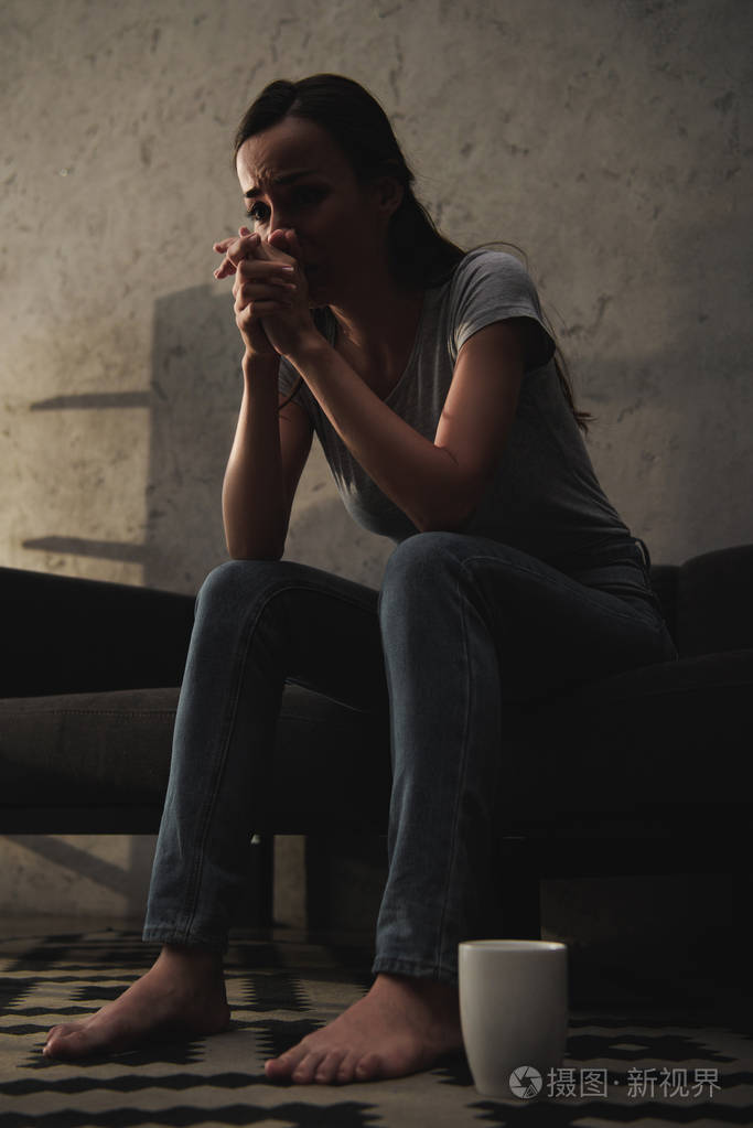 坐在沙发上的哭女人的底部在地板上的咖啡杯