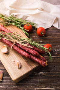 Kabanosy 的传统波兰猪肉香肠在木制的切割板上。还有迷迭香香草大蒜丁香和西红柿浅谈乡土木桌
