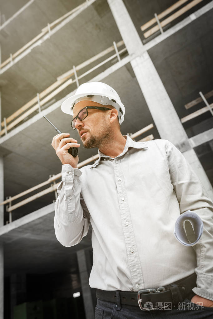 男总工程师戴着白色安全安全帽, 配有对讲机和图纸检查施工现场.