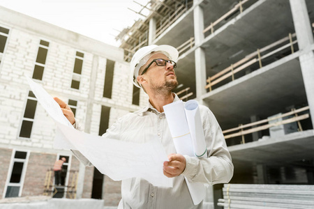 建筑工程师穿着白色的安全帽, 在建筑工地上检查蓝图。发展和建筑业理念