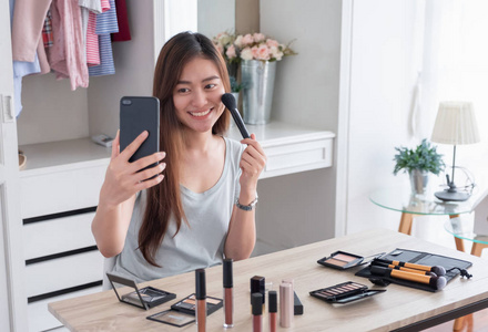 亚洲年轻女性博主录制 vlog 视频使用手机与化妆化妆品在家里的在线影响者对社交媒体的概念。