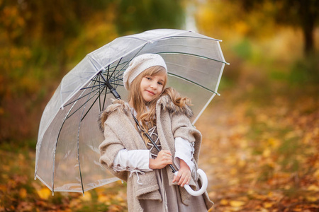 美丽的女孩在复古装备与透明伞散步在秋季公园, 橙色背景, 叶子