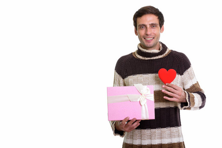 工作室拍摄的快乐的年轻英俊的男子微笑, 同时持有礼品盒和红色的心准备情人节