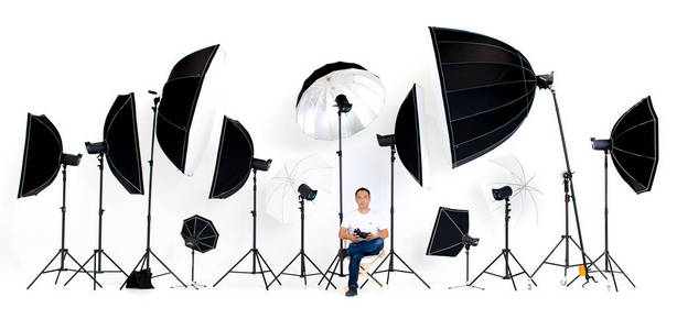 亚洲摄影师坐在导演的椅子上, 闪光灯工作室灯光在白色背景周围的许多模式