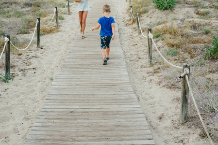 夏天, 孩子们走在木制小路上走向海滩。
