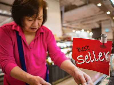 老亚洲妇女购物在超市的畅销书区, 亚洲家庭主妇购物在超级市场