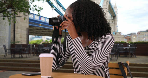 黑人妇女坐在塔桥附近的户外咖啡馆用相机拍照