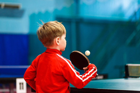 一个孩子在健身房打乒乓球, 一个孩子打网球。