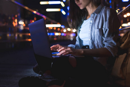 妇女的部分看法使用膝上型电脑在街道与夜城市灯背景