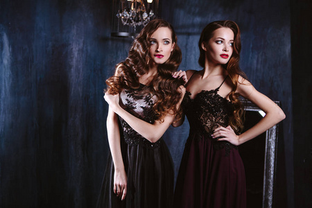 双胞胎年轻妇女在晚礼服, 时尚秀丽画像在黑暗的内部