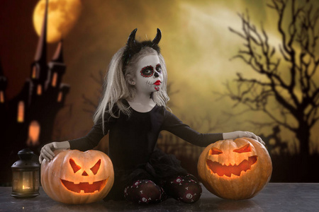 吸血鬼孩子万圣节化妆的小女孩.魔鬼的形象与牛角和南瓜照片