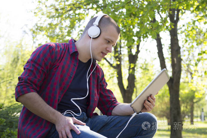 英俊的年轻人坐在公园里, 用平板电脑听音乐。选择性对焦和小景深