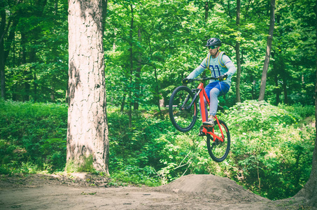 骑自行车头盔上的橙色自行车做一个在跳板跳跃在森林的把戏, 运动模糊