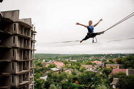 勇敢快乐的女人在 slackline 上的平衡在夏季的高空建筑背景下