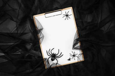 在剪贴板上的空白卡与蜘蛛和网络在黑色背景下