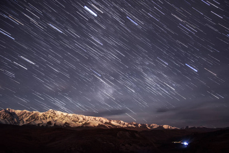 五颜六色的轨道的轨道的形式在星空下的星光夜空的背景下的雪山与背光月亮