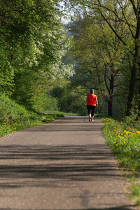 北欧女士穿着红色夹克和灿烂的阳光在春天公园散步, 为快乐运动而照耀