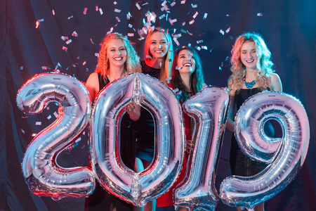 新年派对理念。2019年拿着银色数字并投掷五彩纸屑的年轻妇女团体