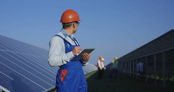 在太阳能电池板中使用平板电脑戴着安全帽的民族工人