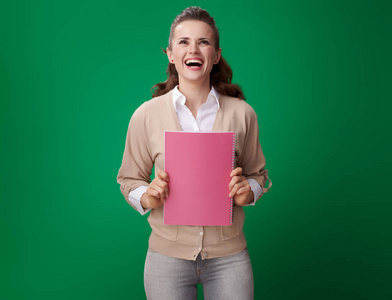 有吸引力的学生妇女粉红色笔记本与粉红色笔记本寻找反对绿色背景