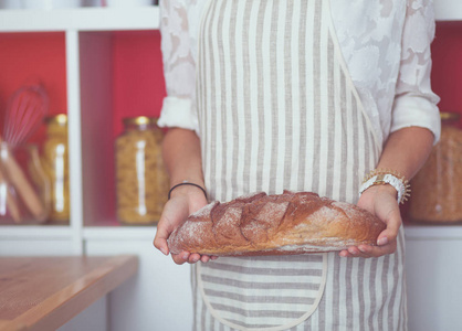一个年轻的妇女站在她的厨房里拿着面包。一个年轻的女人