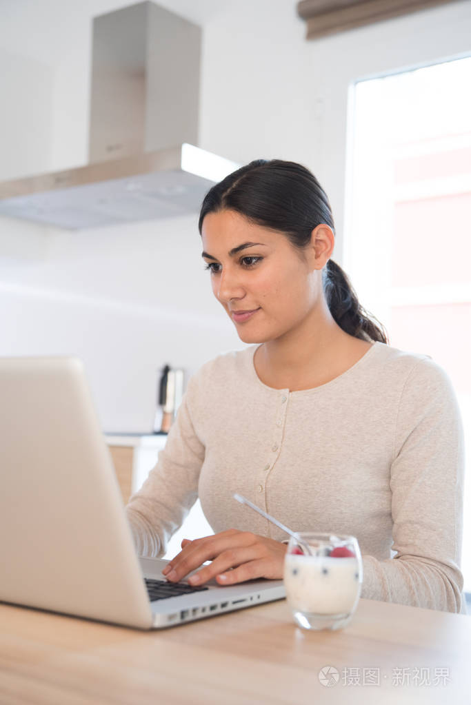 女人坐在桌子前的一个笔记本电脑, 她看着屏幕和打字