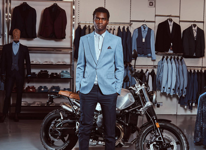 在男装店的复古运动摩托车附近穿着优雅的非洲裔美国年轻人男子